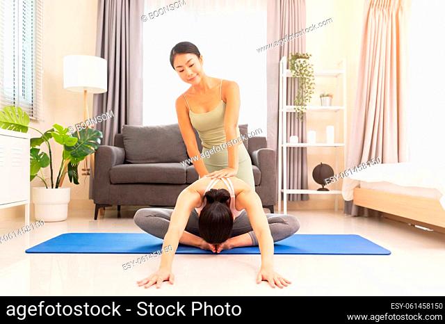 Young woman beginning yoga practice with private teacher at home. Professional instructor teaches student to do Baddha Konasana exercise or Butterfly pose