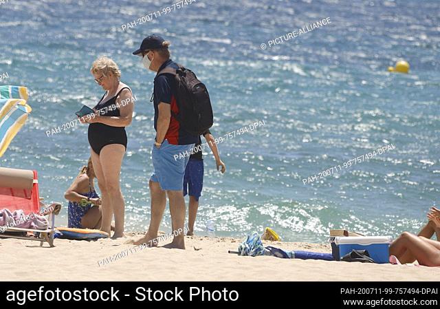 11 July 2020, Spain, Calvia: A man wearing a mouth-and-nose mask is standing on Son Maties beach among the sunbathers. The regional government of the islands...
