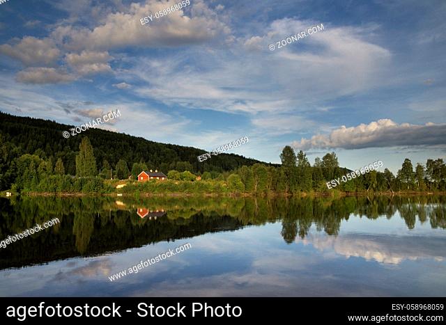 Falured painted house reflecting in the Klaralven river near the Swedish village Branas on a very calm evening