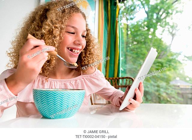 Smiling girl eating breakfast using tablet