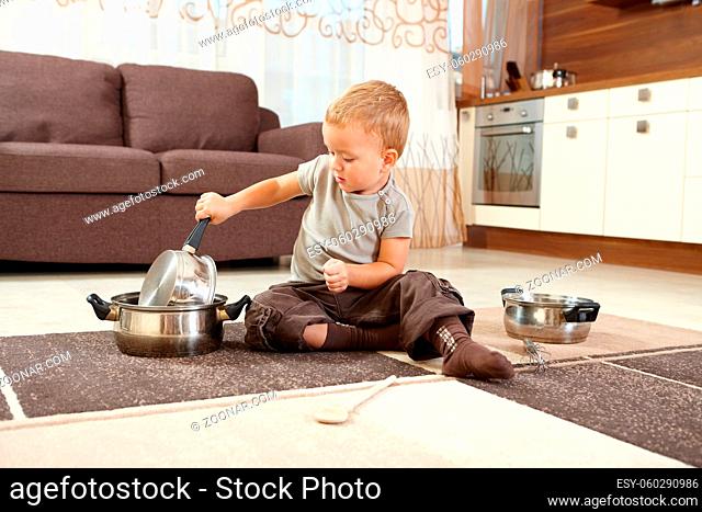 Little boy sitting on carpet in kitchen playing with cooking pots