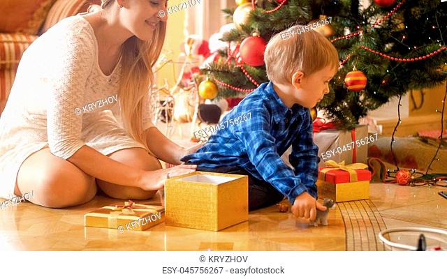 Toddler boy sitting on floor with beautiful young mother under Christmas tree