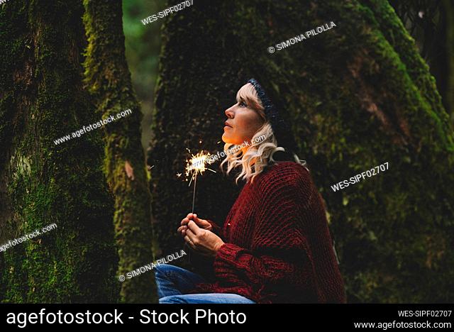 Thoughtful woman holding sparkler in woodland