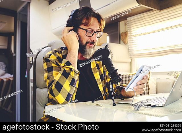 Portrait of young mature man with beard and glasses recording content online with a microphone in alternative van camper office house