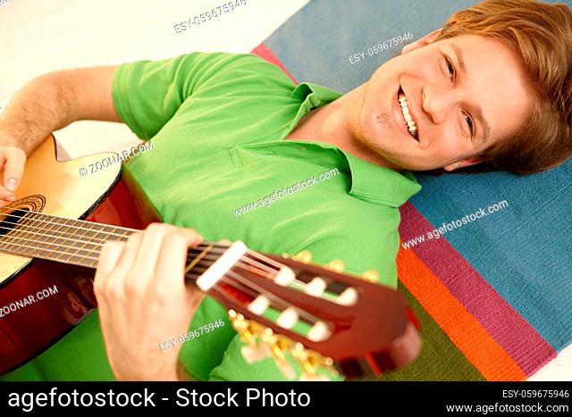 Portrait of handsome guy playing guitar lying on floor