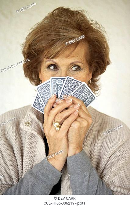 Senior woman holding playing cards over face, close-up