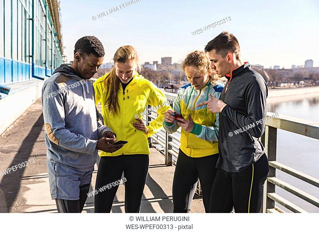 Sportive friends checking cell phones on a bridge in the city