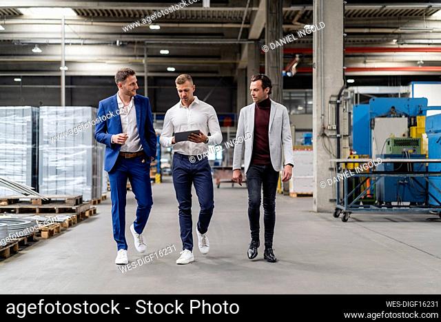 Professional colleagues discussing over digital tablet while walking in factory