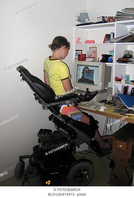 Young woman uses electric wheelchair w/elevating feature to access computer workstation