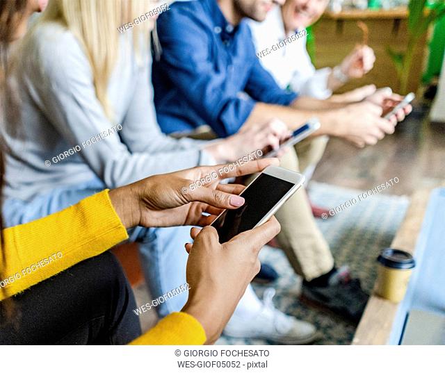 Close-up of business team sitting in loft office using cell phones