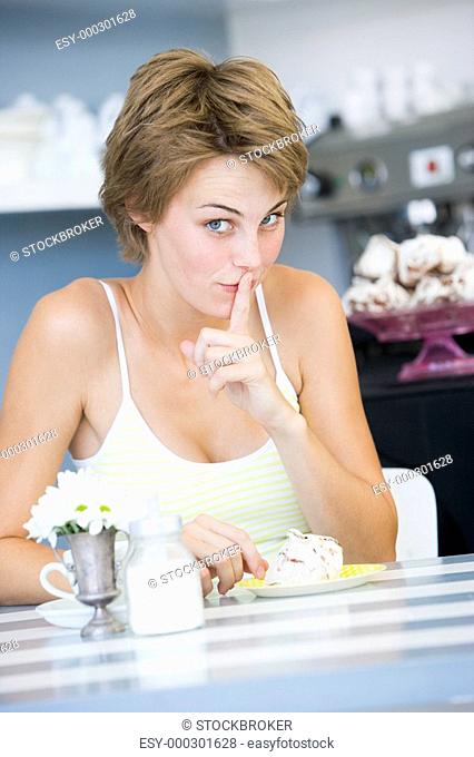 Young woman sitting at a table drinking tea and eating a sweet treat