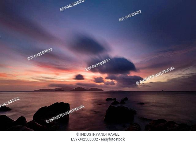 Colorful sunset long exposure with view to Praslin from La Digue, Seychelles with granite rocks in the foreground