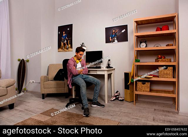 Annoyed teenage boy sitting in his room. View of bored young boy at chair with crossed arms
