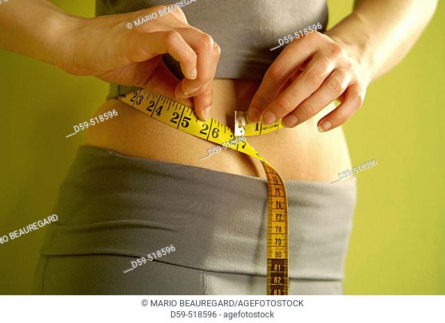 Young woman measuring waistline with tape