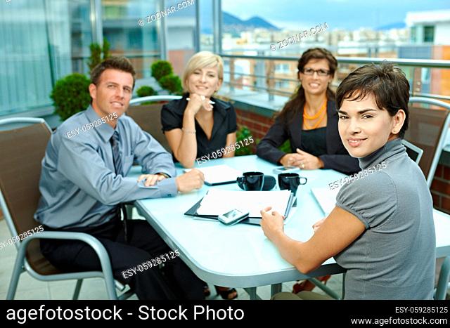 Group of young business people sitting around table on office terrace outdoor, talking and working together
