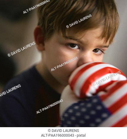 Young boy covering mouth with boxing gloves, portrait