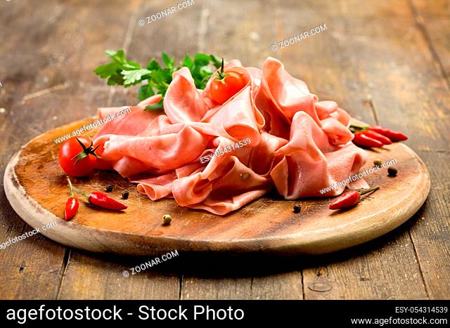 wooden chopping board with sliced mortadella and red pepper