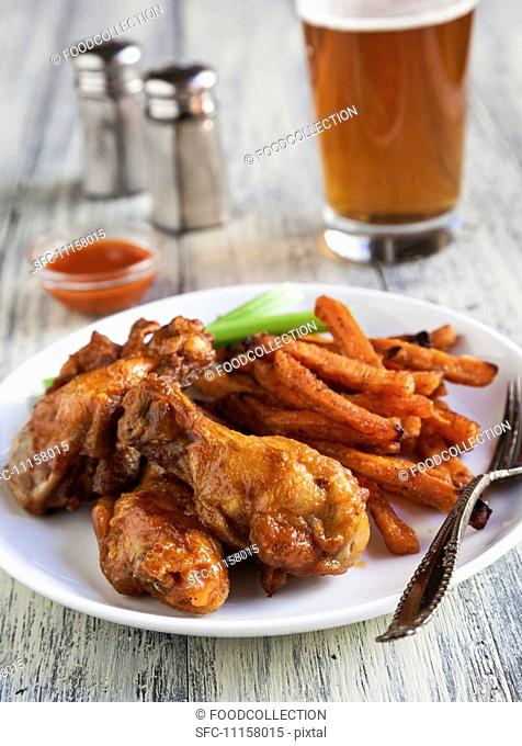 Buffalo Chicken Wings with Sweet Potatoes Fries, Celery Sticks and a Glass of Beer