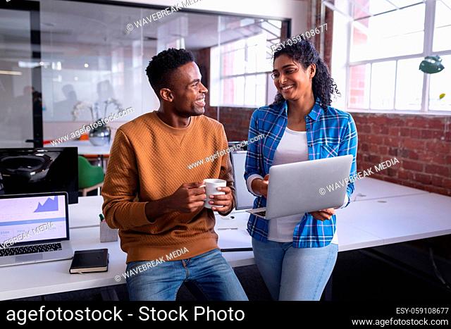 Happy diverse male and female colleagues at work standing discussing in front of laptop