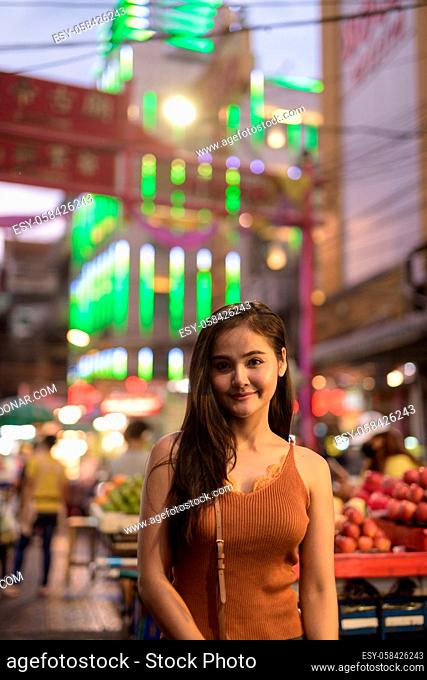 Portrait of young beautiful Asian tourist woman exploring Chinatown in Bangkok city at night