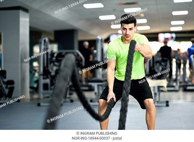 Man with battle ropes exercise in the fitness gym. Young male wearing sportswear