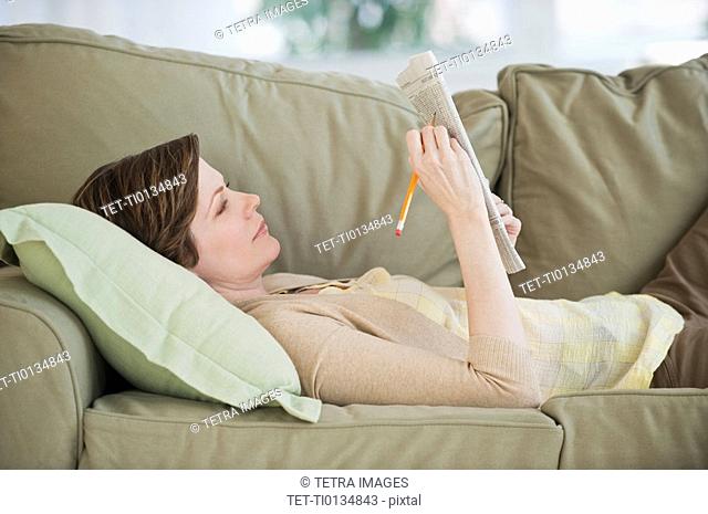 Woman lying on sofa with newspaper