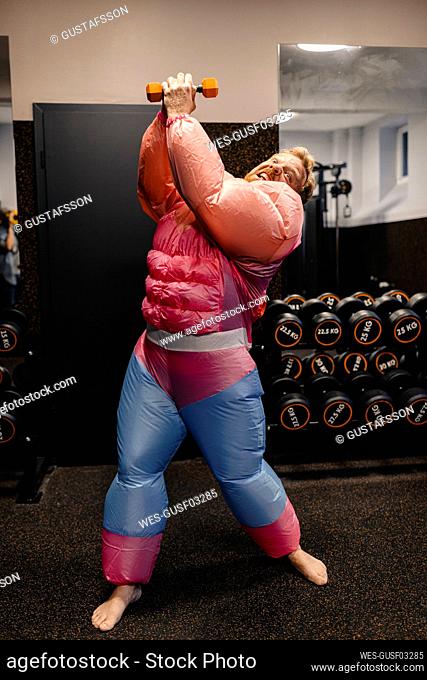 Man in gym wearing pink bodybuilder costume lifting dumbbell