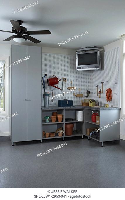 STORAGE: Garage organization, corner, with tv suspended above peg board, open cabinets store gardening tools, closed cabinet to left, ceiling fan, windows