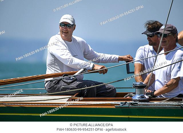 30 June 2018, Germany, Langenargen: King Harald V. of Norway (L) sitting at the tiller of his yacht ""Sira"" during the Aguti Classic Cup