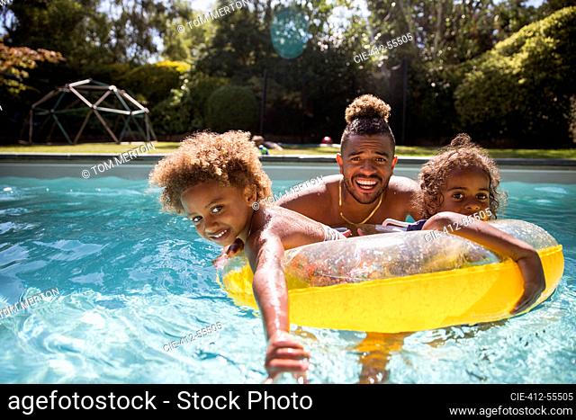 Portrait happy father and daughters playing in sunny swimming pool