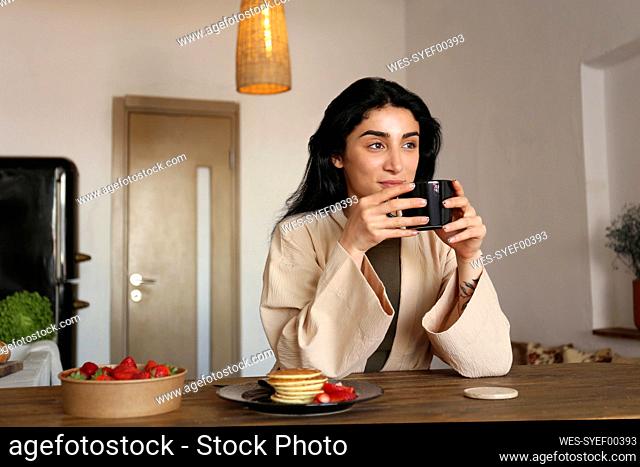 Young woman enjoying brewed coffee with pancakes at table