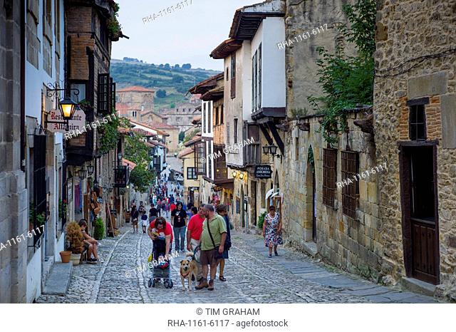 Tourists and residents pass medieval houses in cobbled street of Calle Del Canton in Santillana del Mar, Northern Spain