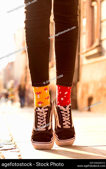 Slim legs of teenage girl wearing different color socks and canvas shoes. Standing on pavement