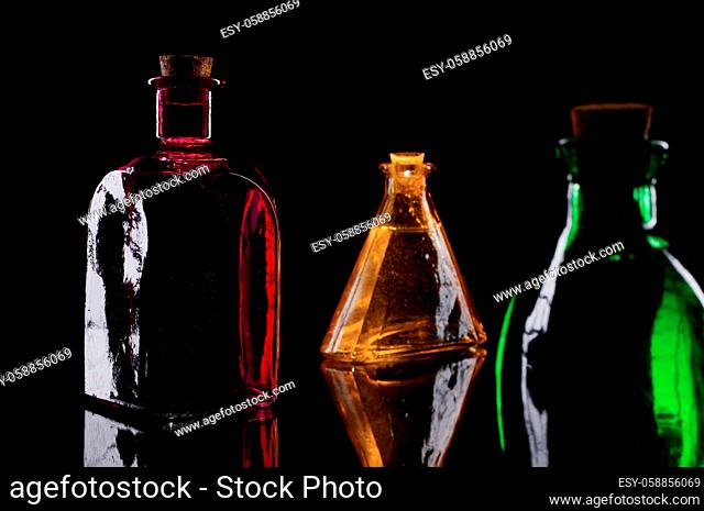 Still life of three colored decorative bottles with corks on glass against black background