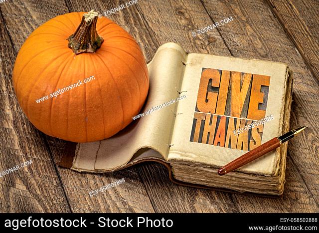 give thanks - word abstract in vintage letterpress wood type in a retro journal with pumpkin against rustic wood, Thanksgiving concept