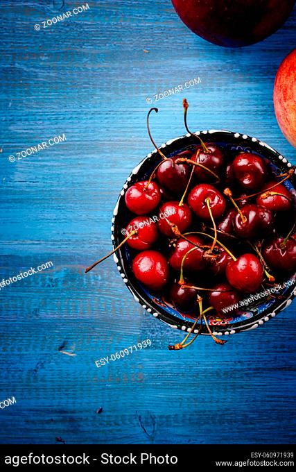 Apples and a bowl with a cherry on a blue wooden countertop