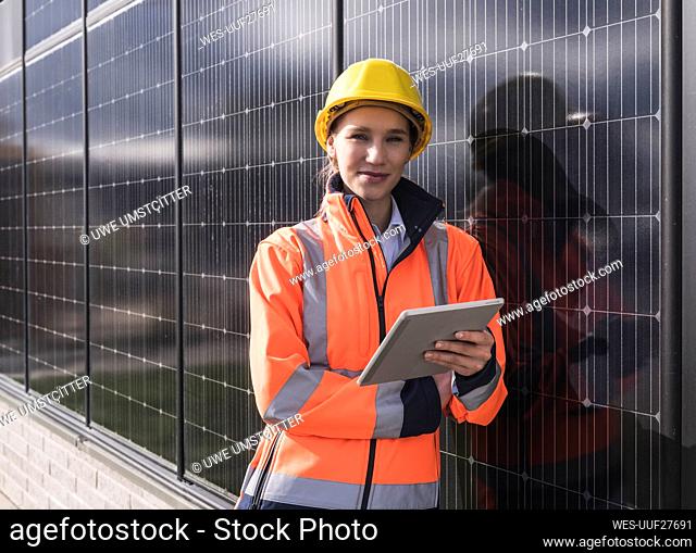 Smiling female engineer with tablet PC leaning on solar panels