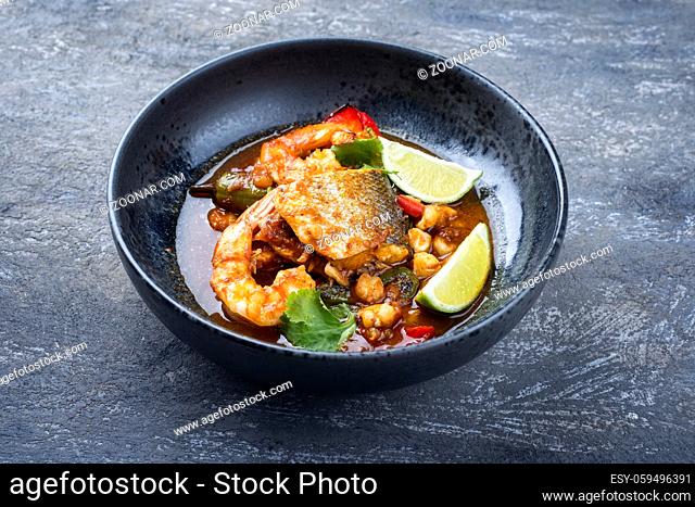 Modern style traditional Mexican seafood pozole soup with fish, king prawns and hominy in a clear sauce served as close-up in design bowl