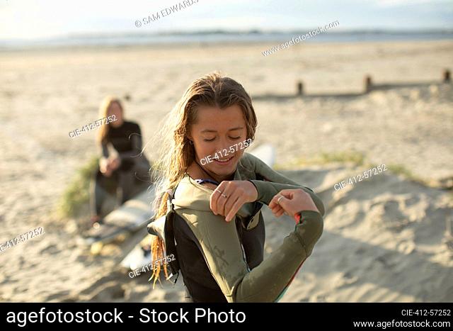Surfista de sexo femenino joven que pone en traje de neopreno en la playa soleada de verano