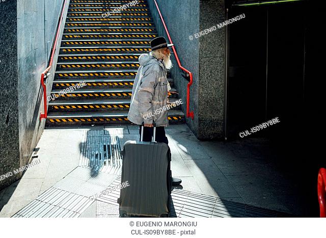 Senior man with wheeled luggage entering subway, Milano, Lombardia, Italy