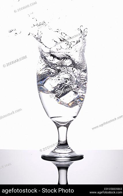 A studio photo of ice being dropped into a glass of water against a white background