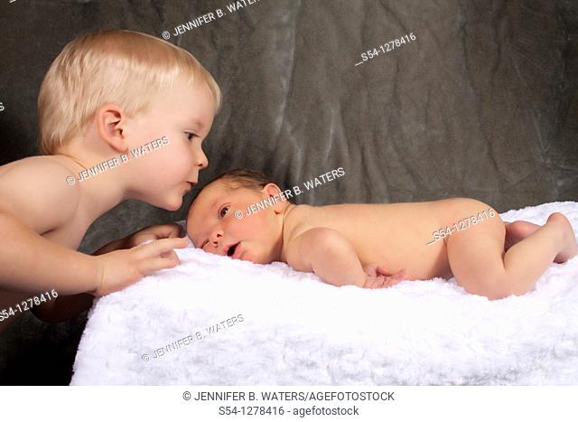 A two year old boy kisses his newborn baby brother