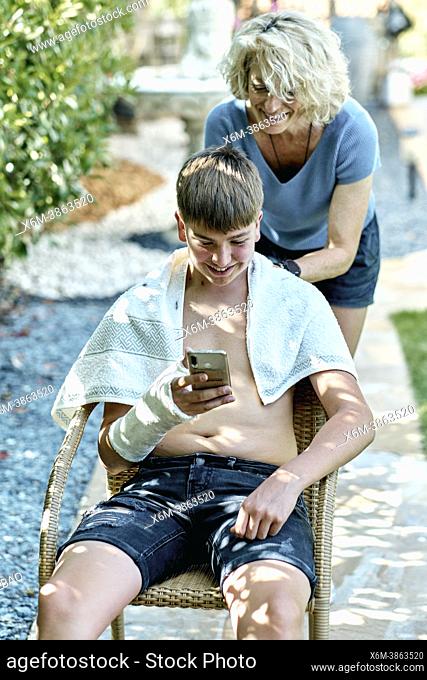 Portrait of a mother cutting young caucasian boy's hair outside in a garden. Lifestyle concept