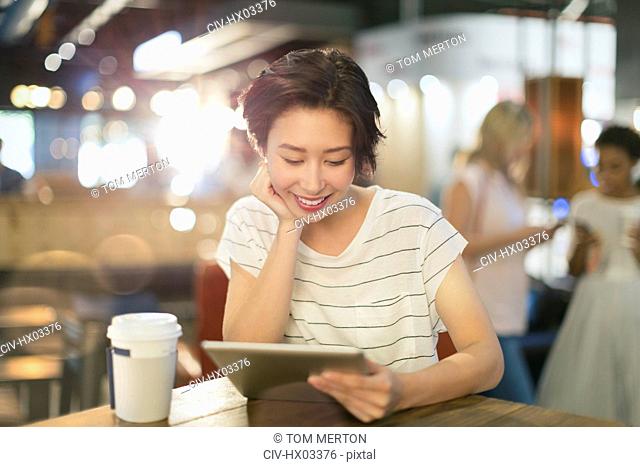 Young woman using digital tablet and drinking coffee in cafe