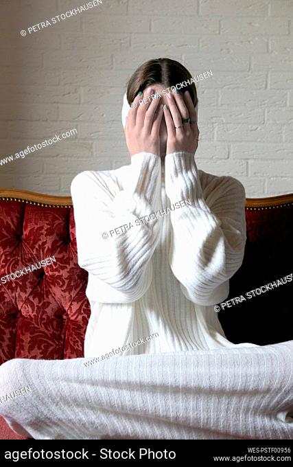 Teenage girl covering face with hands on sofa