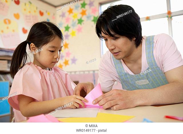 Kindergarten Teacher and Girl Playing Origami