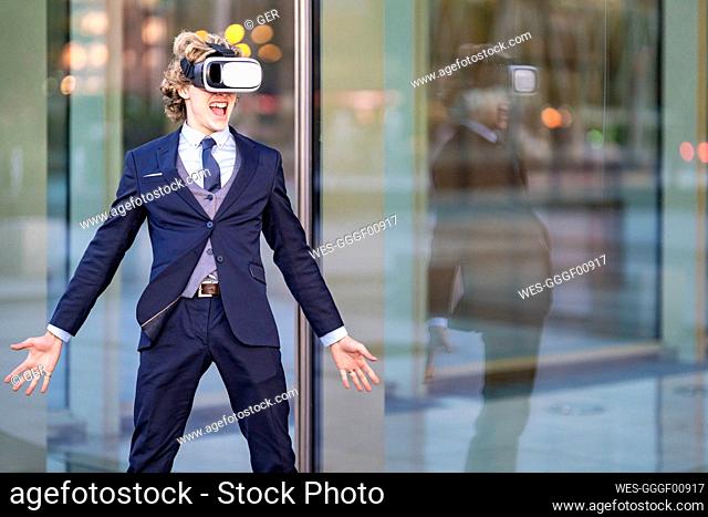 Excited male entrepreneur screaming while wearing VR Box against office building