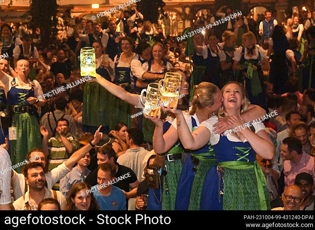 03 October 2023, Bavaria, Munich: Waiters celebrate the end of the Wiesn with illuminated steins and the guests at the traditional Kehraus in the Hofbräuzelt
