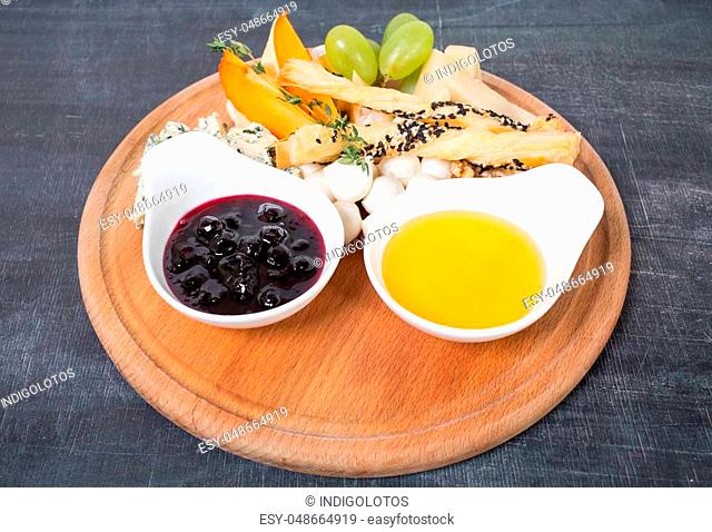 Cheese platter with honey and berry jam. Plate located on a black table as a background