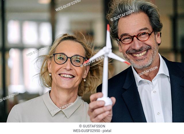 Portrait of happy businessman and businesswoman holding wind turbine model in office